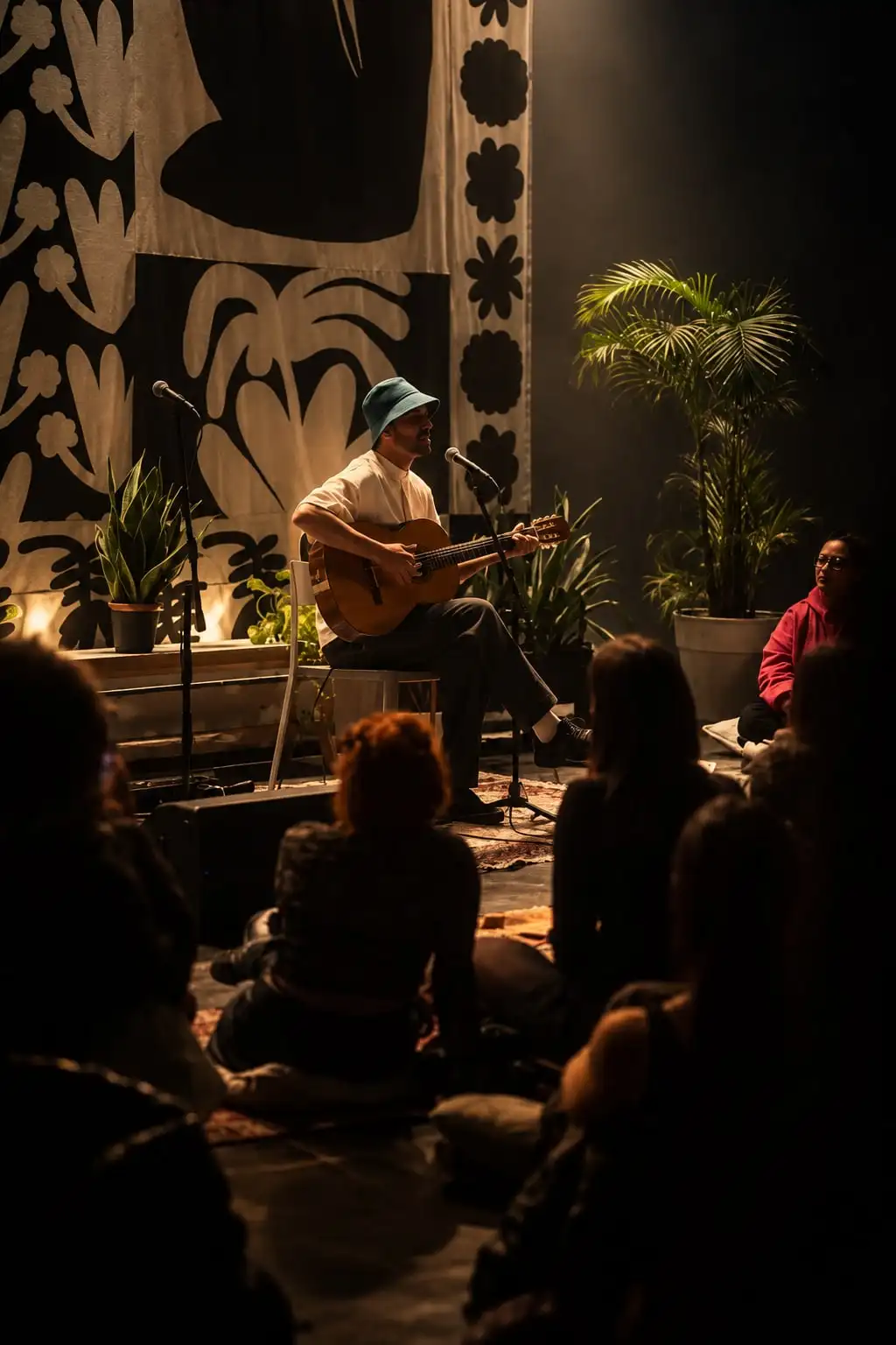 Un músico de gorro toca la guitarra frente al público sentado en el piso, entre plantas.