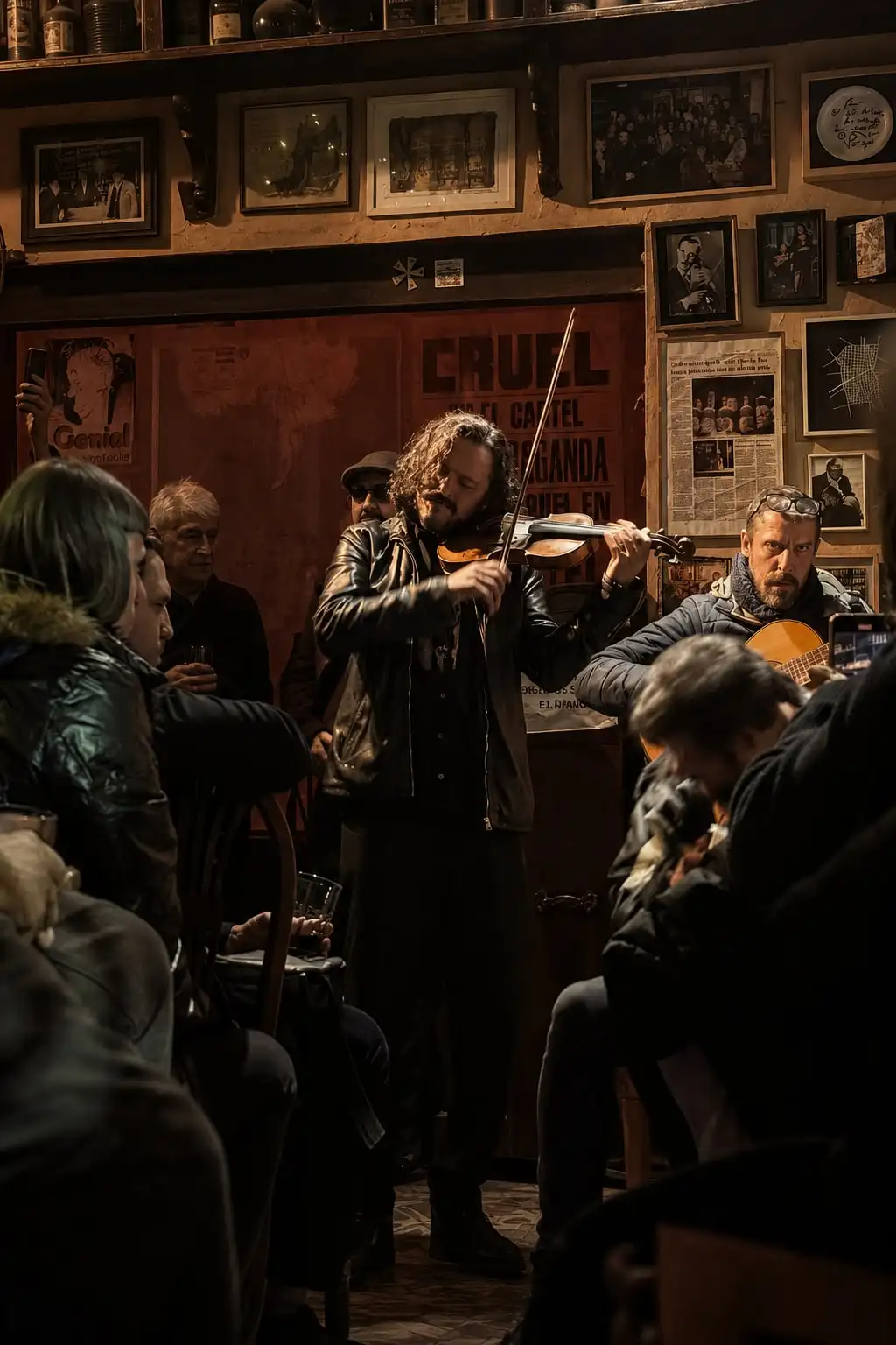 Un violinista y un guitarrista tocan entre el público, en un bar con las paredes cubiertas de cuadros.