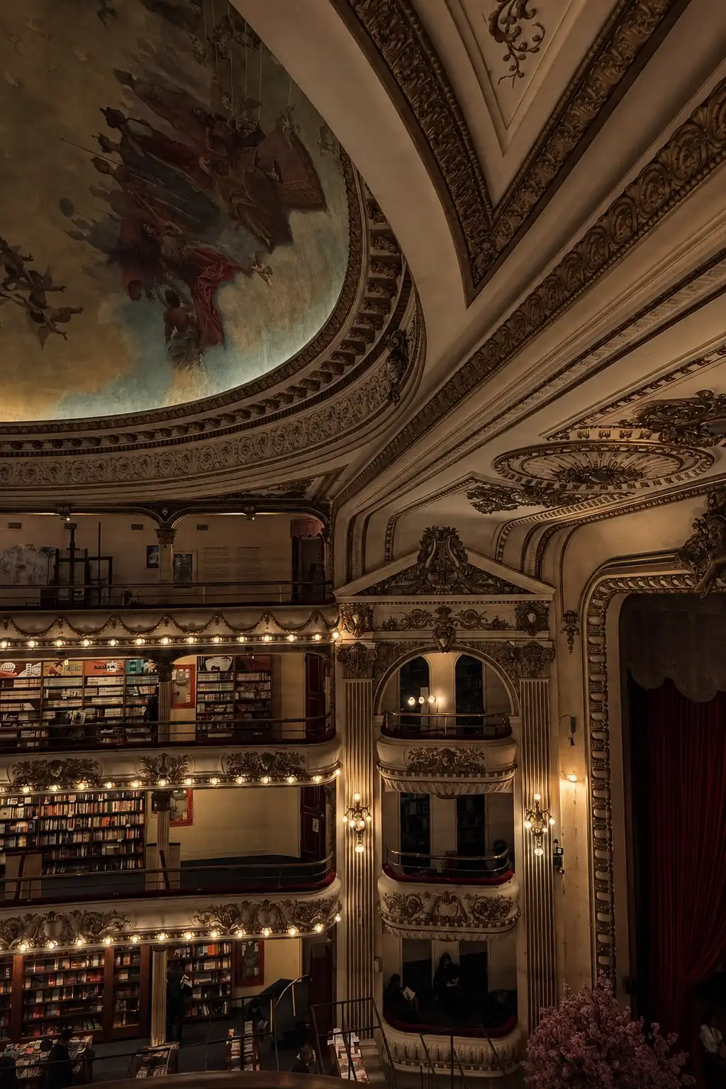Interior de un teatro antiguo convertido en librería: palcos iluminados llenos de estantes y una cúpula pintada.