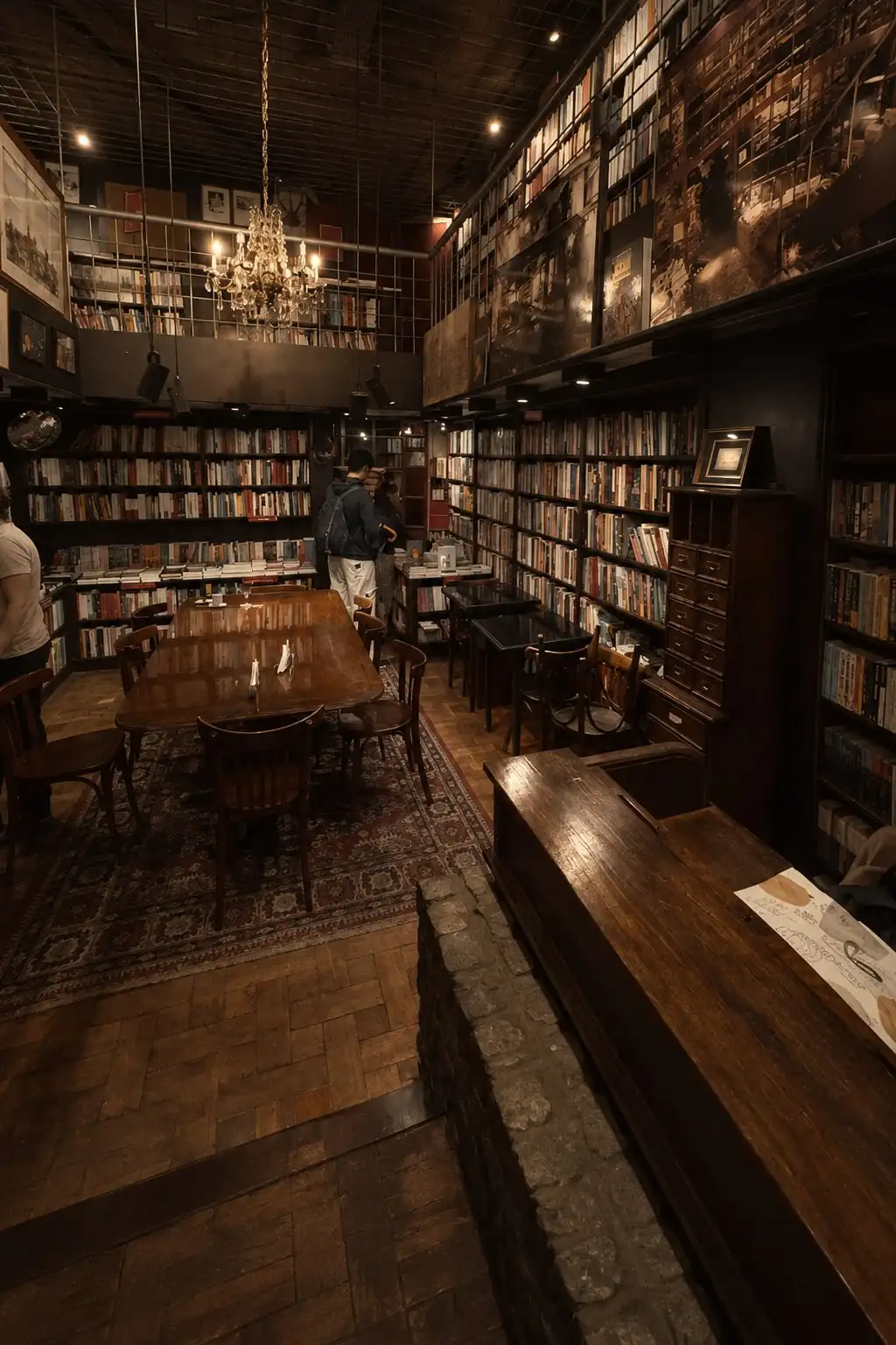 Salón de madera oscura con paredes de libros hasta el techo, una araña y mesas de café.
