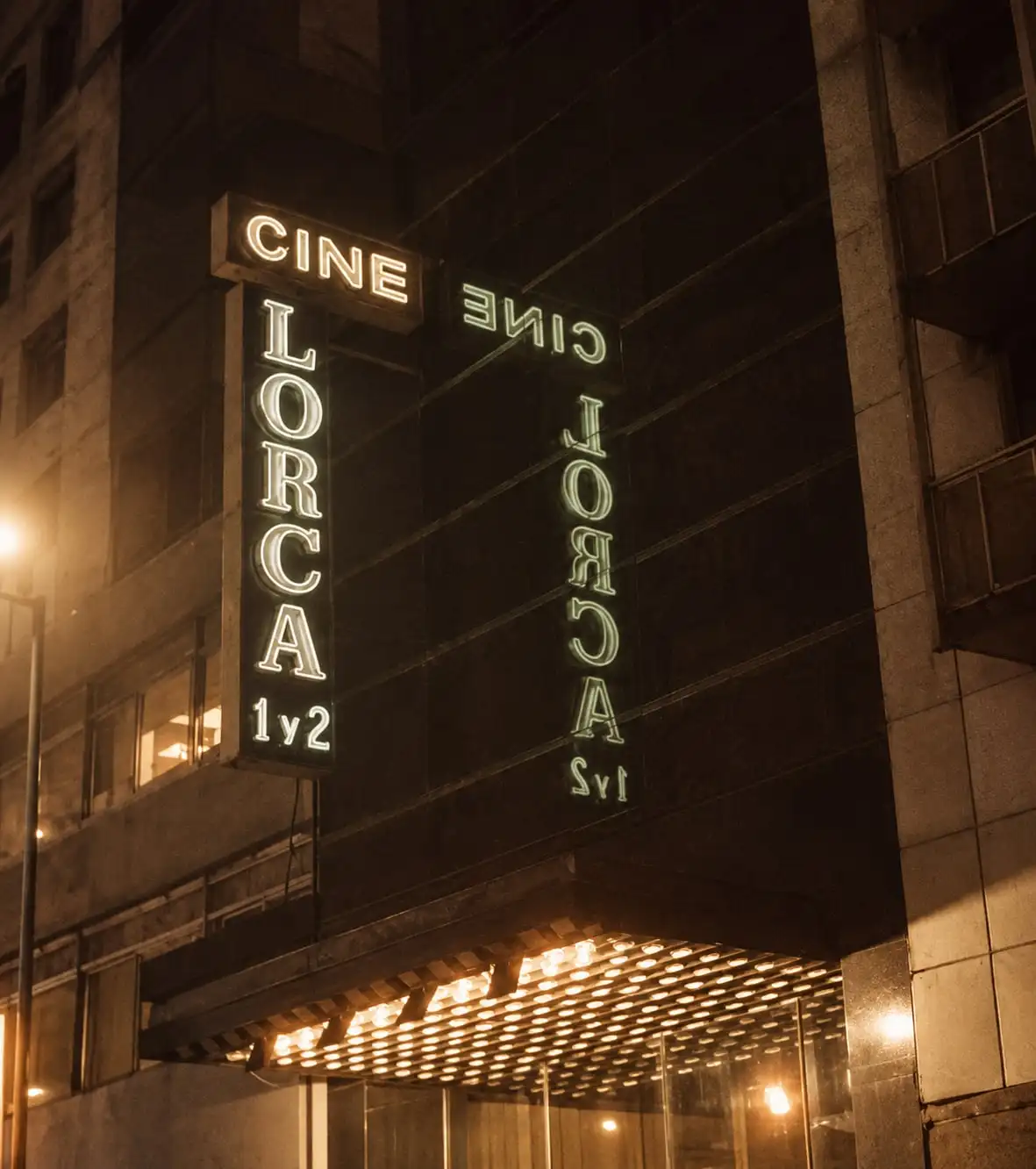 El cartel vertical iluminado «Cine Lorca 1 y 2» sobre la marquesina, de noche.
