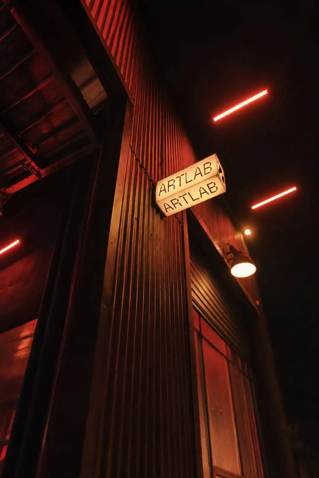 Fachada oscura de noche con un cartel luminoso que dice «Artlab» y líneas de neón rojo.