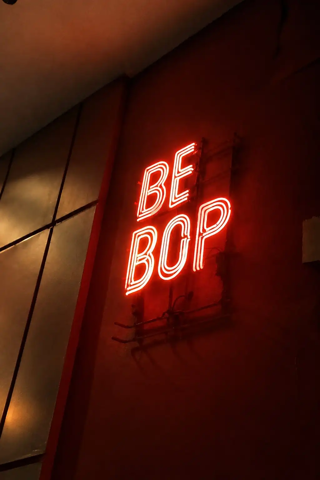 Cartel de neón rojo que dice «Be Bop» sobre una pared oscura.