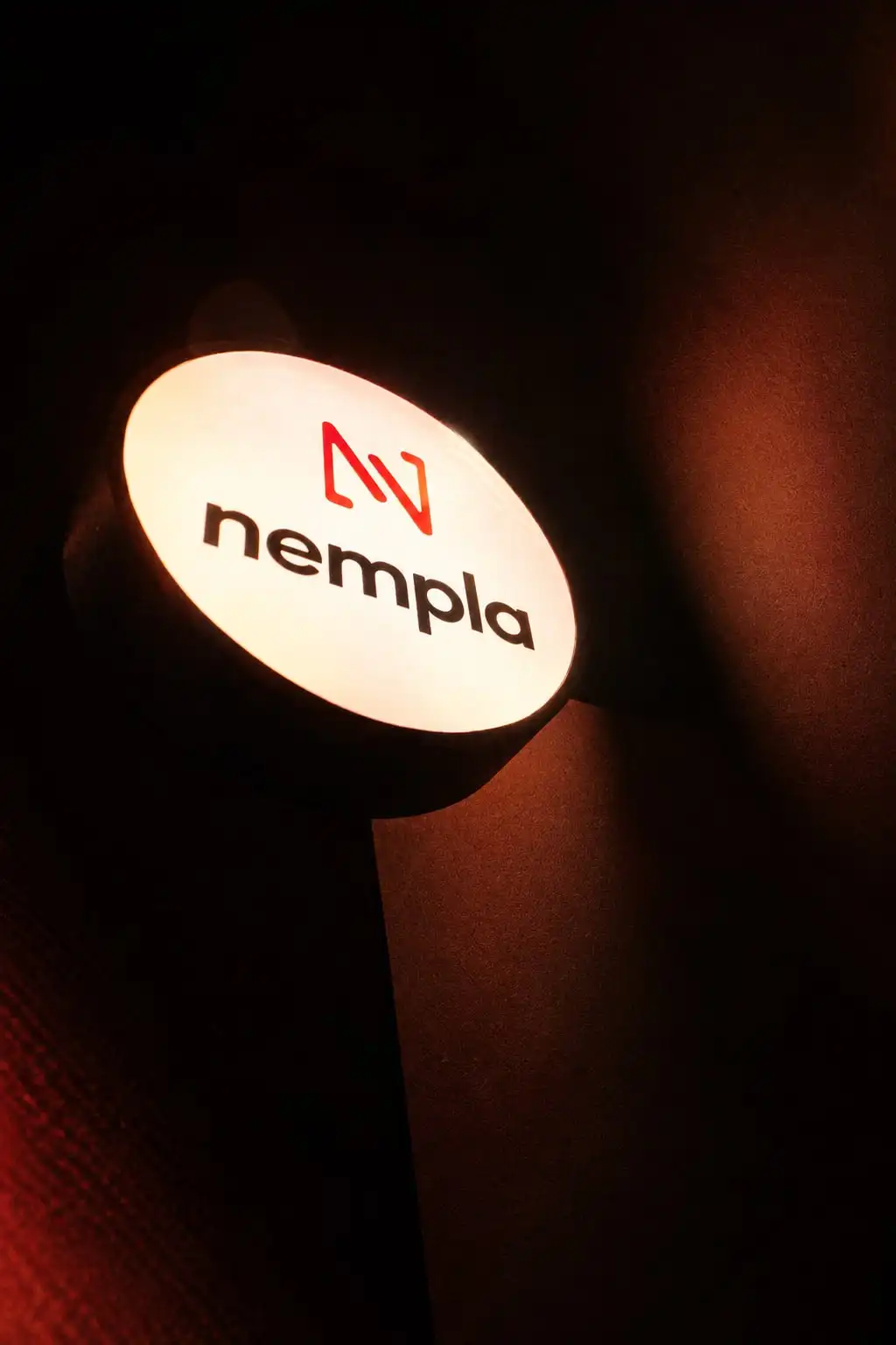 Cartel redondo iluminado con el logo de Nempla sobre una pared oscura.