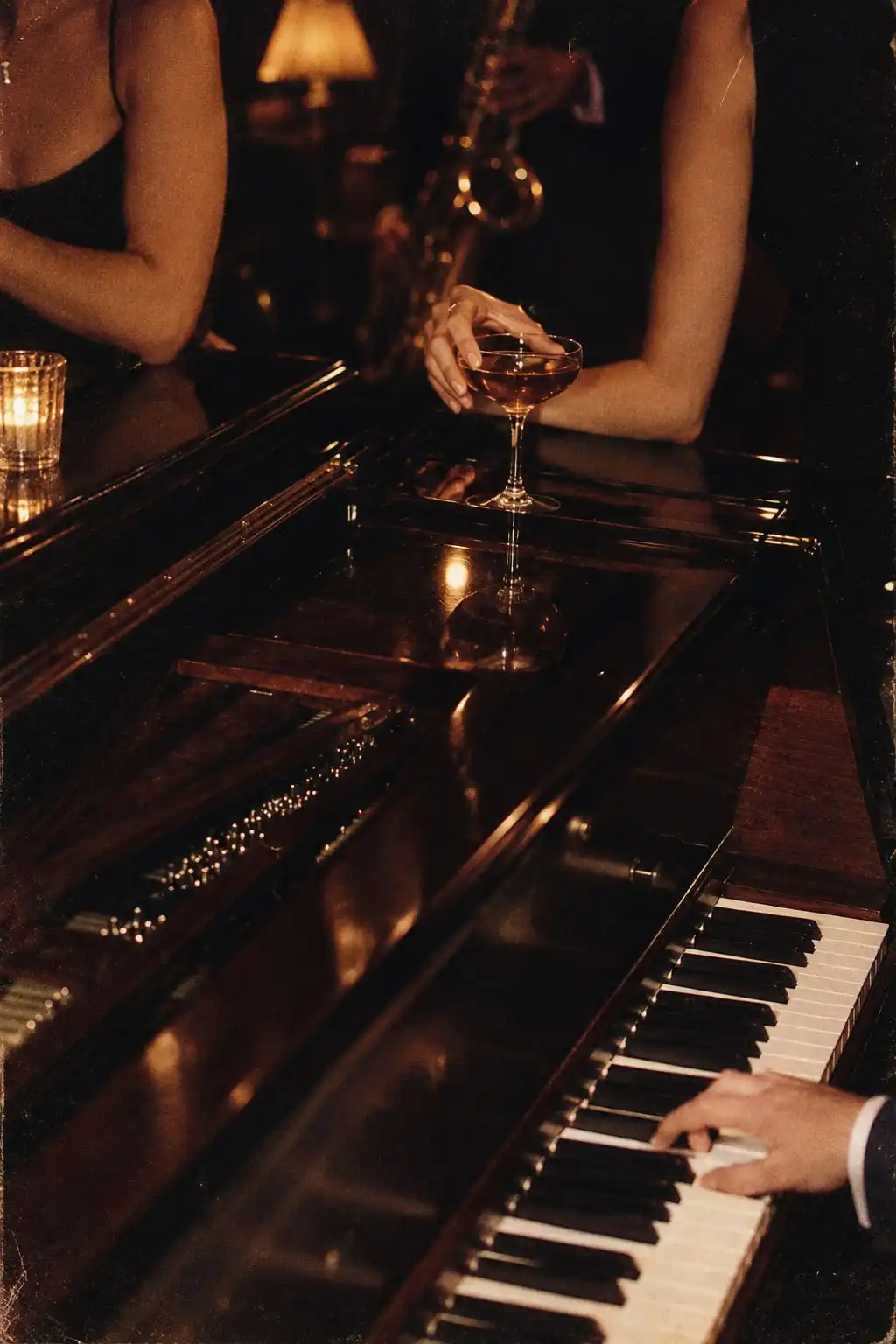 Las manos de un pianista sobre el teclado de un piano de cola; apoyada en la tapa, una copa, y detrás un saxofón a media luz.