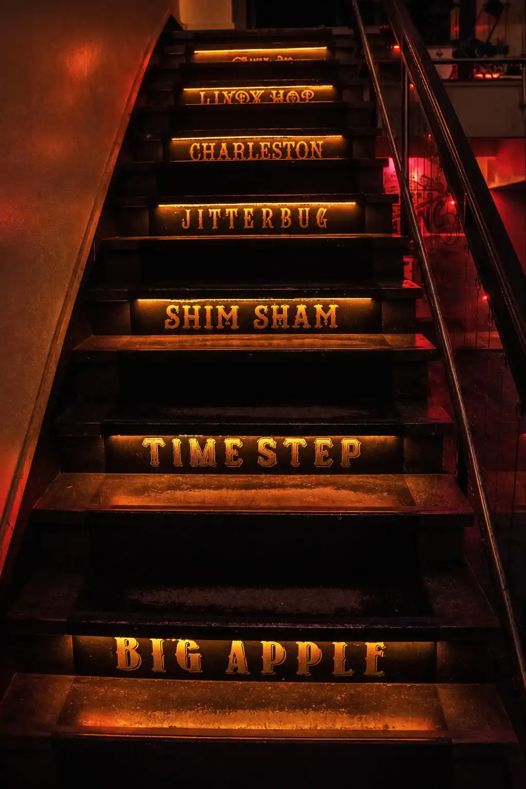 Escalera con nombres de pasos de swing iluminados en cada escalón: Charleston, Jitterbug, Shim Sham, Big Apple.